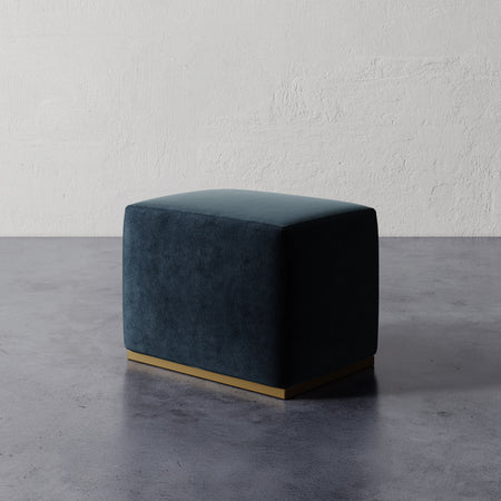 Lemieux et Cie Sophie Rectangular Ottoman in deep teal upholstery with base detail, compact ottoman on concrete floor against textured plaster wall.