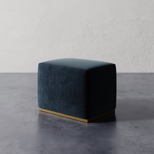Lemieux et Cie Sophie Rectangular Ottoman in deep teal upholstery with base detail, compact ottoman on concrete floor against textured plaster wall.