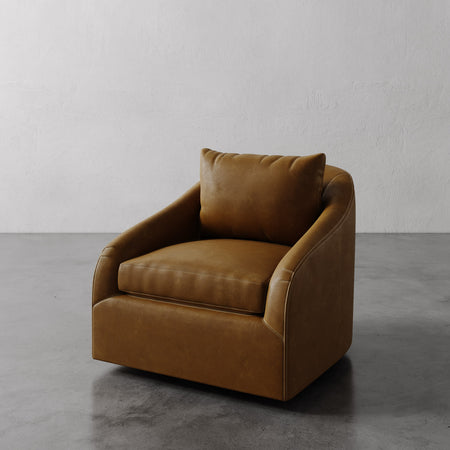 Lemieux et Cie Rousseau Swivel Chair in warm caramel leather, low-profile lounge chair with rounded arms, shown on concrete floor against white plaster wall.