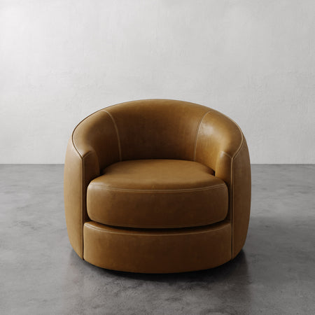 Lemieux et Cie Rulmann Swivel Chair in warm tan leather, rounded barrel-back chair with sculptural form, shown on concrete floor.
