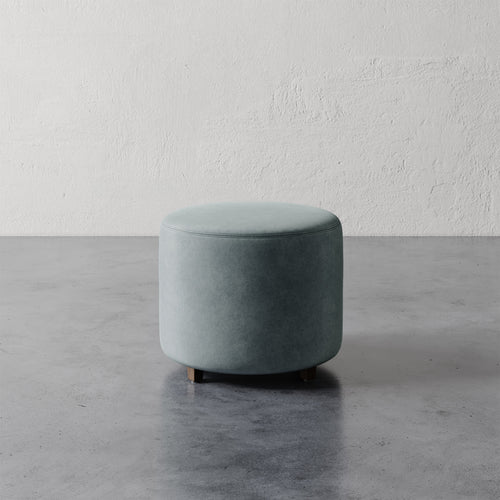 Lemieux et Cie Fabien 22" Round Ottoman in seafoam upholstery, low cylindrical ottoman on concrete floor against textured plaster walls
