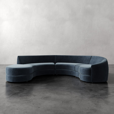 Lemieux et Cie Rulmann 4-Piece Right Sectional in slate blue, curved modular sofa on polished concrete floor against neutral plaster walls.