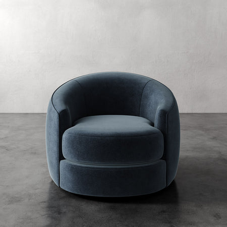 Lemieux et Cie Rulmann Swivel Chair in deep charcoal, rounded sculptural form with curved arms, on polished concrete floor against textured plaster wall.