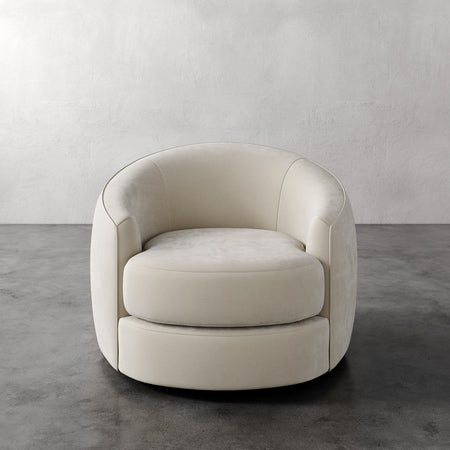 Lemieux et Cie Rulmann Swivel Chair in ivory, rounded barrel-back form with sculptural curves, on polished concrete floor against textured plaster wall.