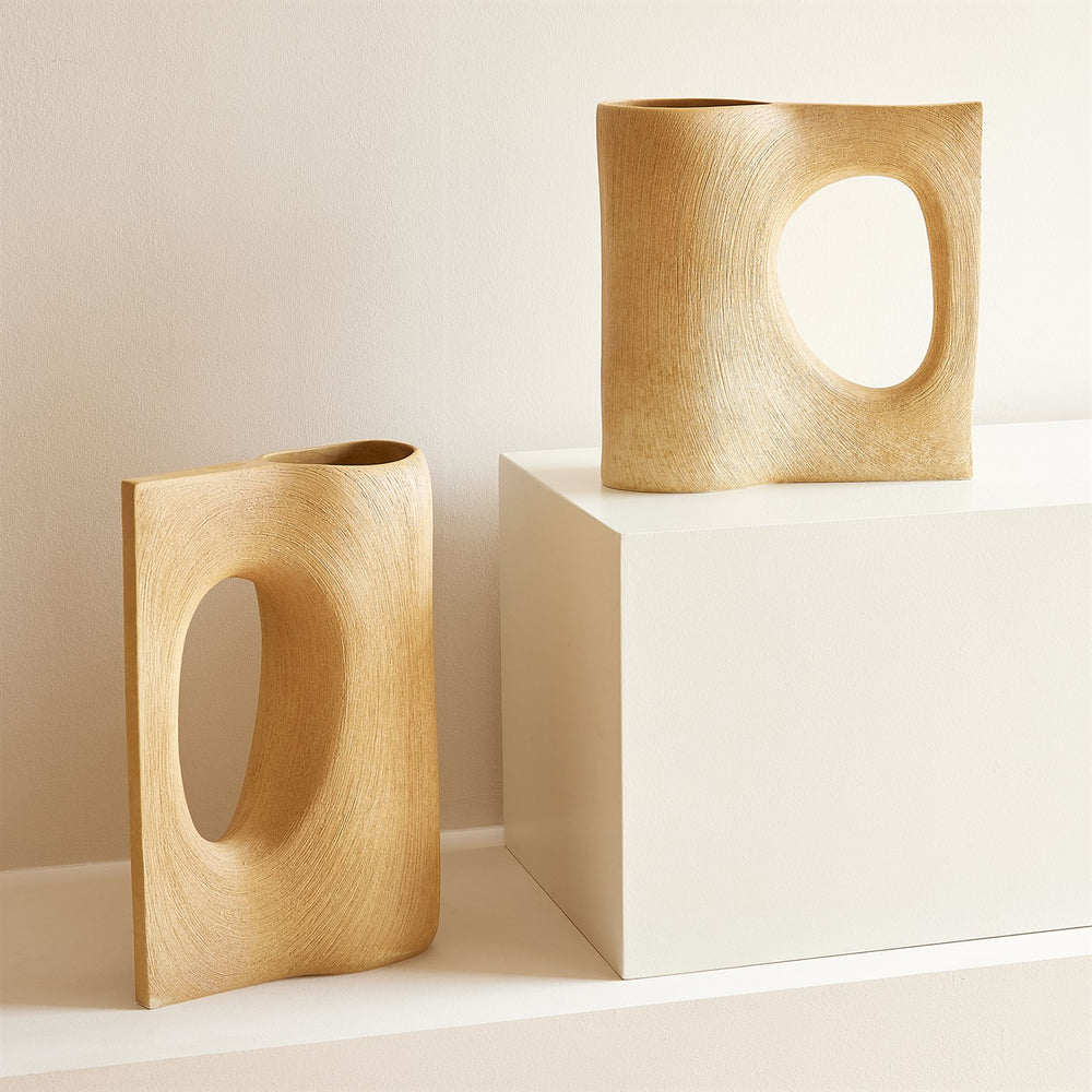 Lemieux et Cie Moreau Vase in vintage brass, sculptural shell-form vessels with organic cutouts, displayed on neutral pedestals against warm plaster walls.