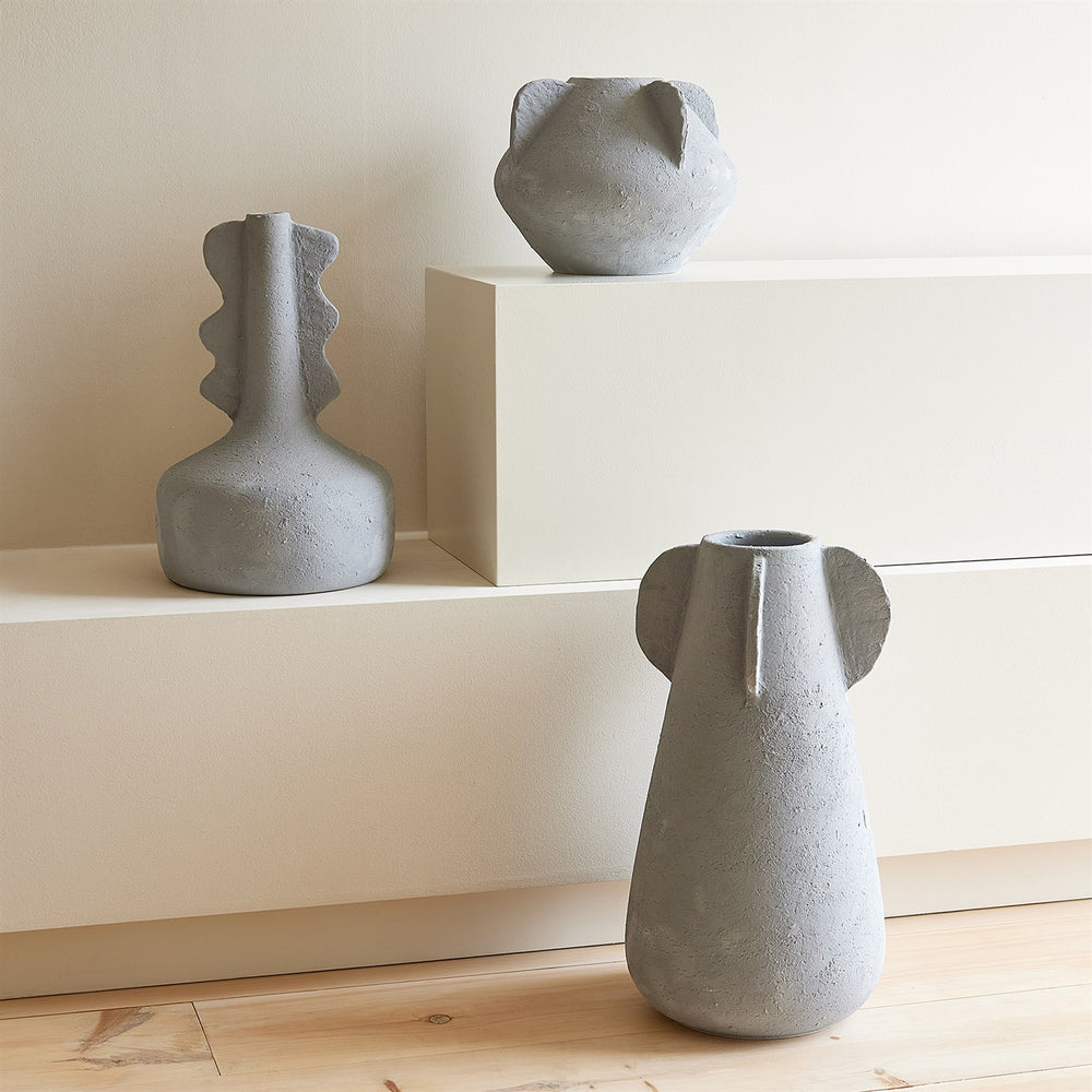 Lemieux et Cie Anouar Vase Collection in grey, sculptural vessels with organic textured forms, displayed on neutral shelves and wood flooring.