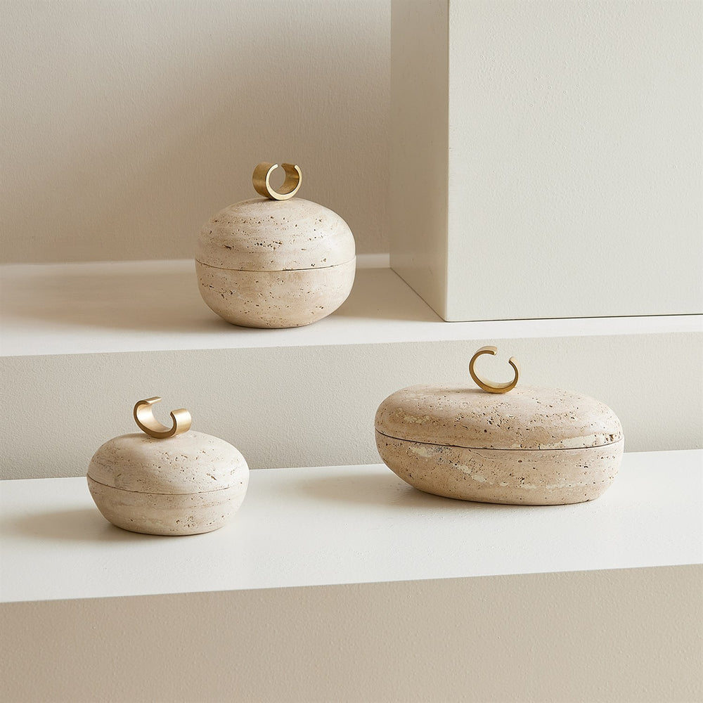 Lemieux et Cie Caillou Lidded Pot in travertine with brass sculptural handle, organic rounded forms on neutral plaster ledge.