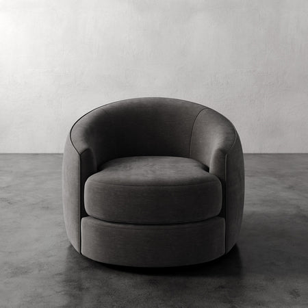 Lemieux et Cie Rulmann Swivel Chair in charcoal, rounded barrel-back lounge chair on concrete floor against textured plaster walls.