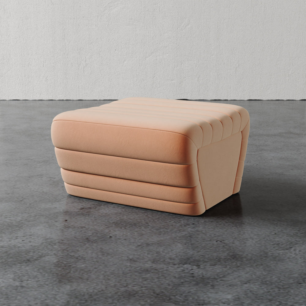 Lemieux et Cie Brunoy Ottoman in blush upholstery, sculptural channeled ottoman on stone floor against textured plaster walls.