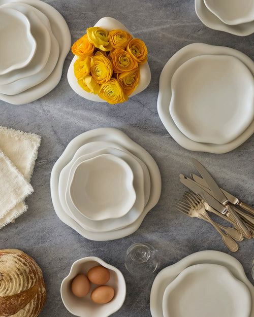 Lemieux et Cie Amorphous Pasta Bowl Set in ivory, tableware styled with yellow ranunculus, artisan bread, and flatware on gray stone surface.