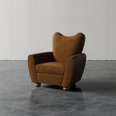 Lemieux et Cie Danielle Chair in warm tan leather, sculptural curved wingback form with rounded feet, on polished concrete floor against textured plaster wall.