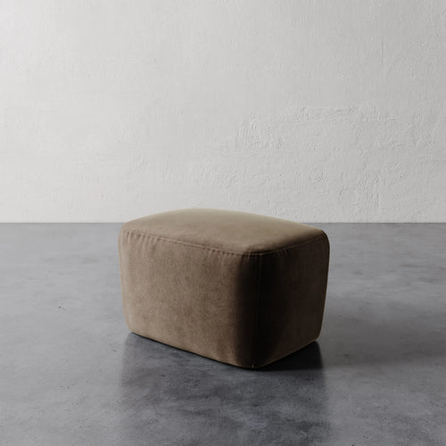 Lemieux et Cie Aurélie Ottoman in warm taupe, low-profile rectangular ottoman on concrete floor against textured plaster walls.