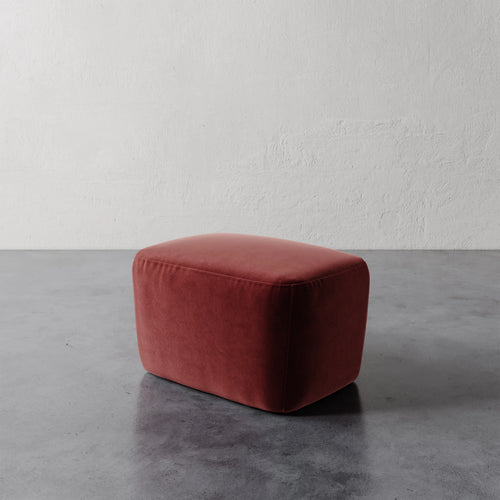 Lemieux et Cie Aurélie Ottoman in terracotta, low rectangular ottoman shown on polished concrete floor against textured plaster wall.