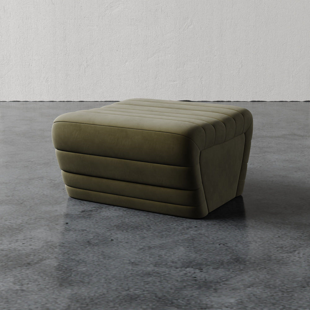 Lemieux et Cie Brunoy Ottoman in olive green with channel-tufted upholstery, low-profile ottoman on polished concrete flooring against textured plaster walls.