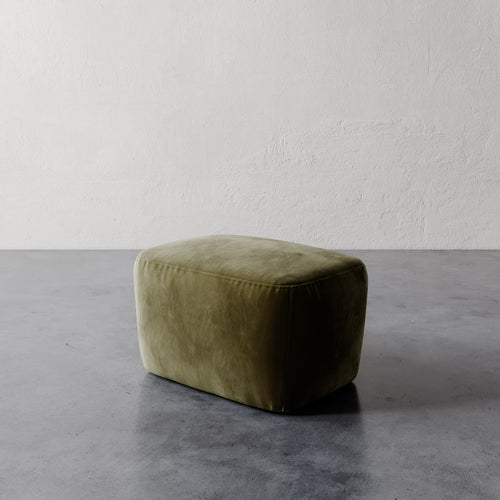 Lemieux et Cie Aurélie Ottoman in olive green, rounded low-profile ottoman on concrete floor against textured white plaster walls.