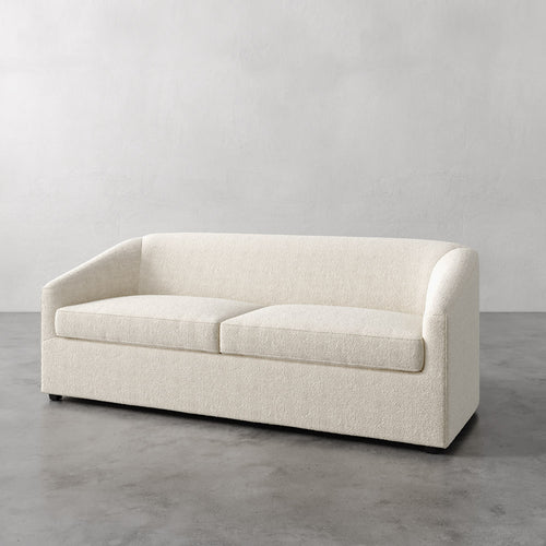 Lemieux et Cie Arvelle Queen Sleeper in ivory, curved-arm sofa with clean lines, shown on concrete floor against neutral plaster walls.