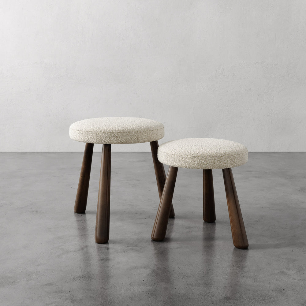 Lemieux et Cie Madeleine Stool with hand-upholstered circular seat and tapered legs, pair of stools shown on polished concrete floor against neutral plaster walls.