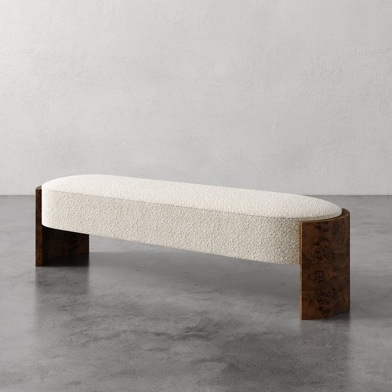 Lemieux et Cie Benoit Bench in cream upholstery with curved maple burl legs, upholstered bench on polished concrete floor against textured plaster walls.