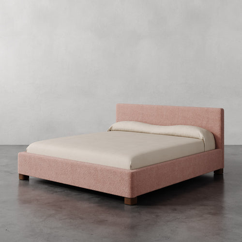 Lemieux et Cie Gérard Bed in blush bouclé, low-profile platform bed with wrapped headboard, shown on polished concrete floor against neutral plaster walls.