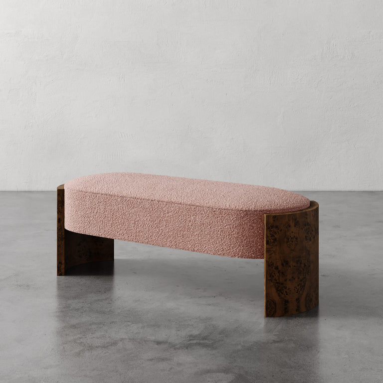 Lemieux et Cie Benoit Custom Upholstered Bench in blush bouclé with curved Maple burl legs, shown on polished concrete floor against white plaster wall.