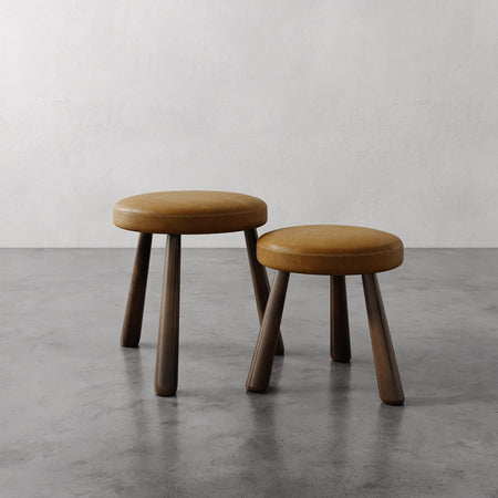 Lemieux et Cie Madeleine Leather Stool in tan leather with tapered legs, sculptural stools shown on polished concrete floor against white plaster wall.