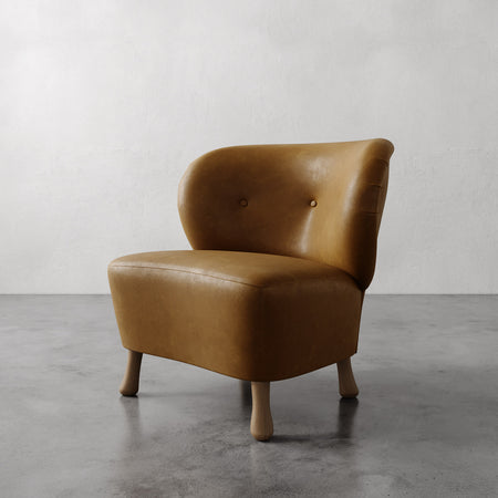 Lemieux et Cie Tourenne Chair in warm tobacco leather, low-profile slipper chair with rounded back and turned legs, on concrete floor.