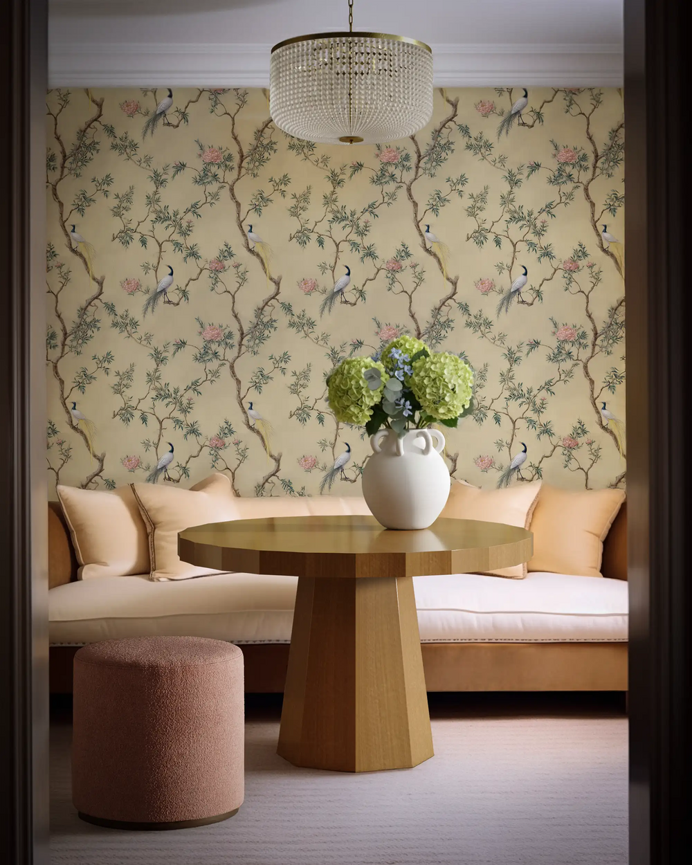 Lemieux et Cie Botanical Gold Wallpaper in celadon green with chinoiserie bird motif, shown behind upholstered seating and beaded chandelier in warm sitting room.