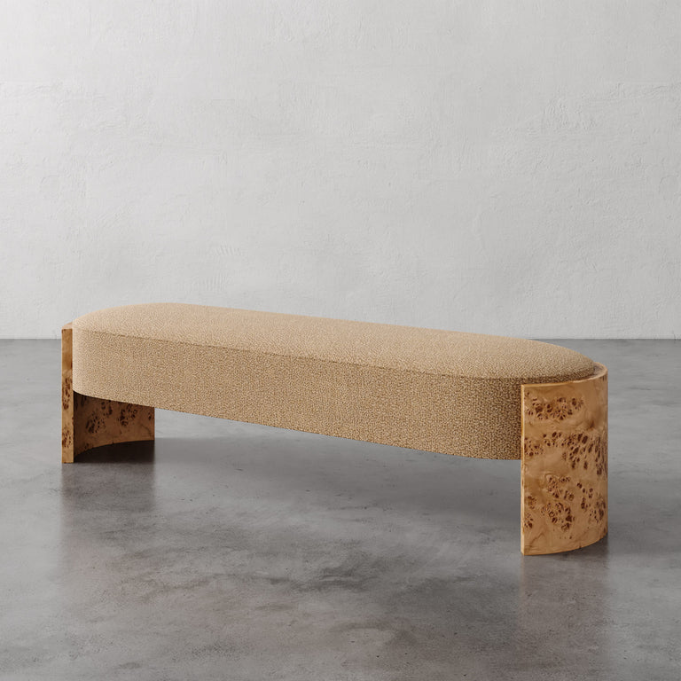 Lemieux et Cie Benoit Custom Upholstered Bench in neutral bouclé with curved Maple burl legs, shown on polished concrete floor against textured plaster walls.