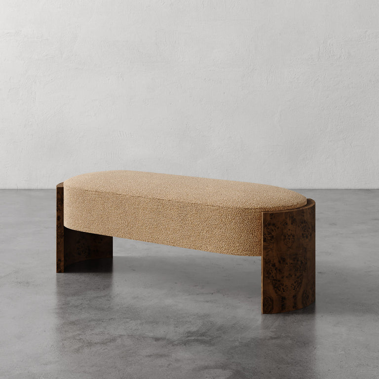 Lemieux et Cie Benoit Bench in textured upholstery with curved Maple burl legs, low-profile seating on concrete floor against textured plaster walls.