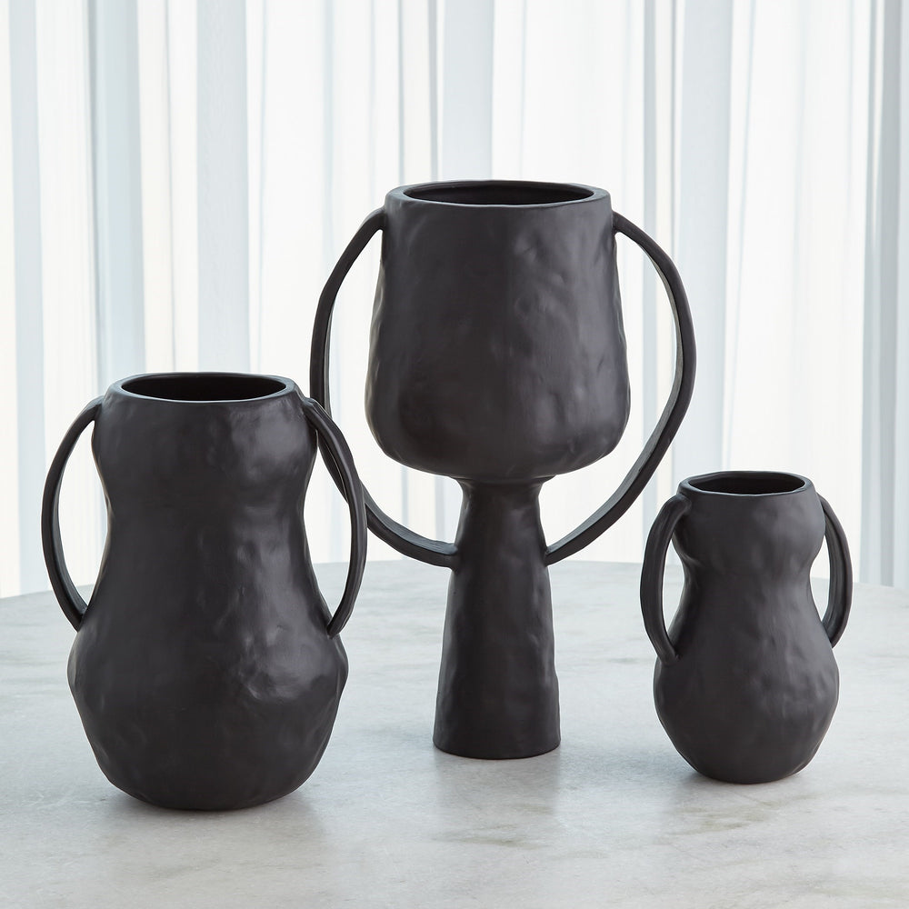 Lemieux et Cie Aquitaine Vase set in matte black with ribbon handles, sculptural vessels shown in three sizes on stone surface with white pleated backdrop.