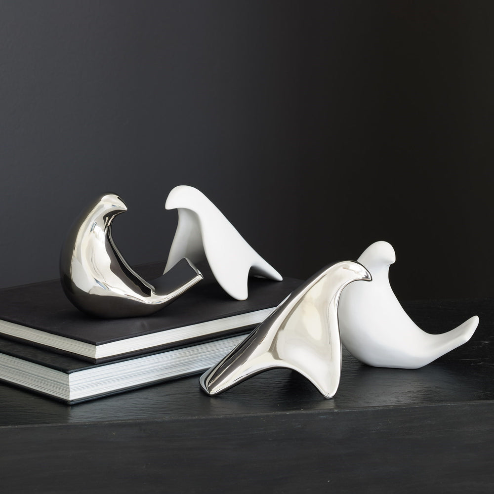 Lemieux et Cie bird objects, sculptural forms with polished finish, styled on dark wood surface with stacked books and charcoal backdrop.