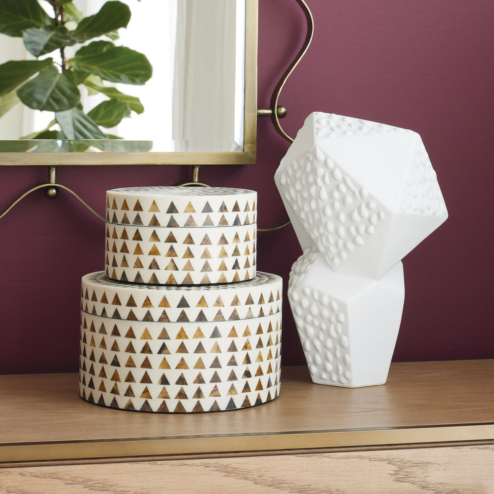Lemieux et Cie hand-carved sculptural vase in white, geometric form with textured surface, styled on wood surface with warm plum walls and mirror.