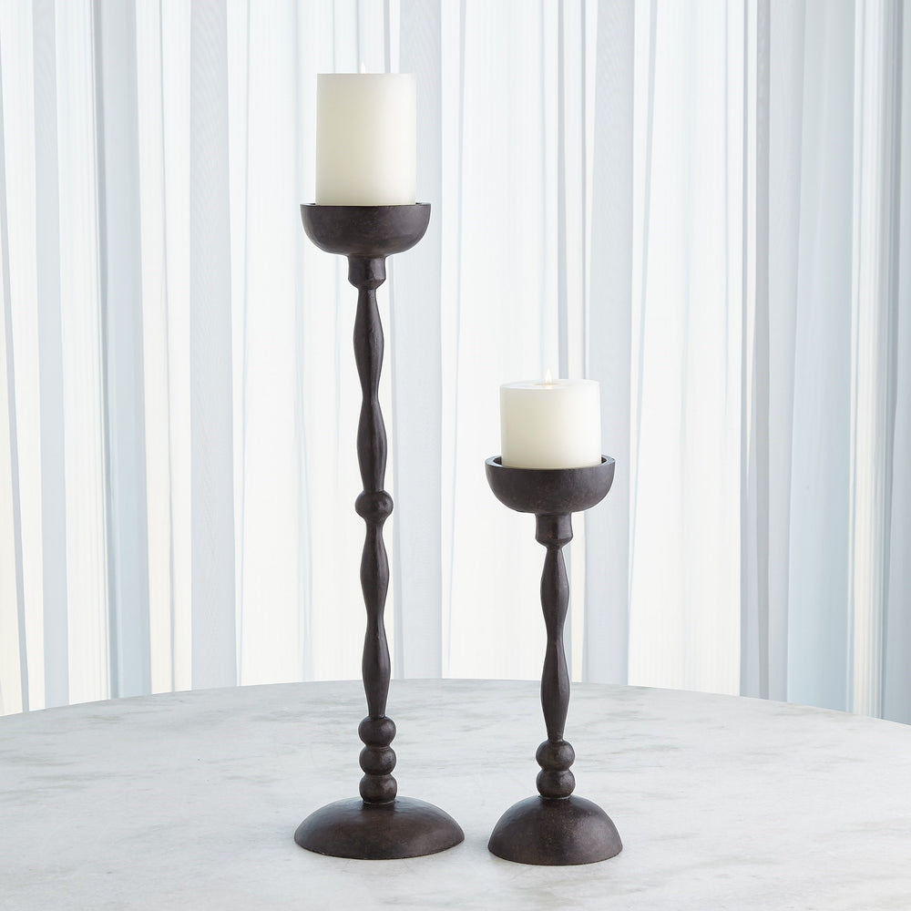 Lemieux et Cie Achille Candle Holder, hand-forged dark finish candlesticks with turned stems and shallow cups, styled on stone surface against white paneled walls