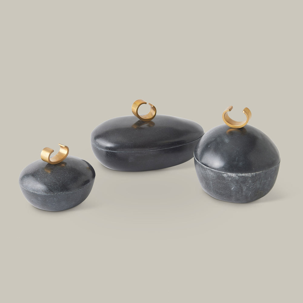 Lemieux et Cie Caillou Lidded Pots in black marble, organic rounded vessel forms with curved brass handles, shown on neutral studio backdrop.