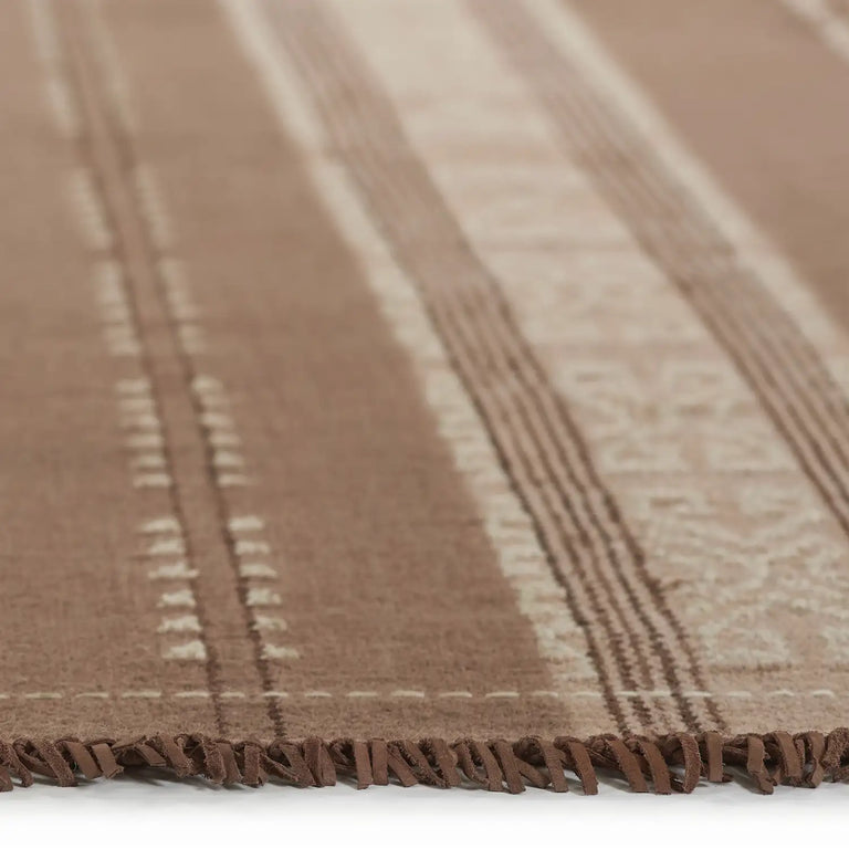 Lemieux et Cie Beaunay rug detail in warm taupe with linear striping, handwoven textile with knotted edge, shown on white studio backdrop