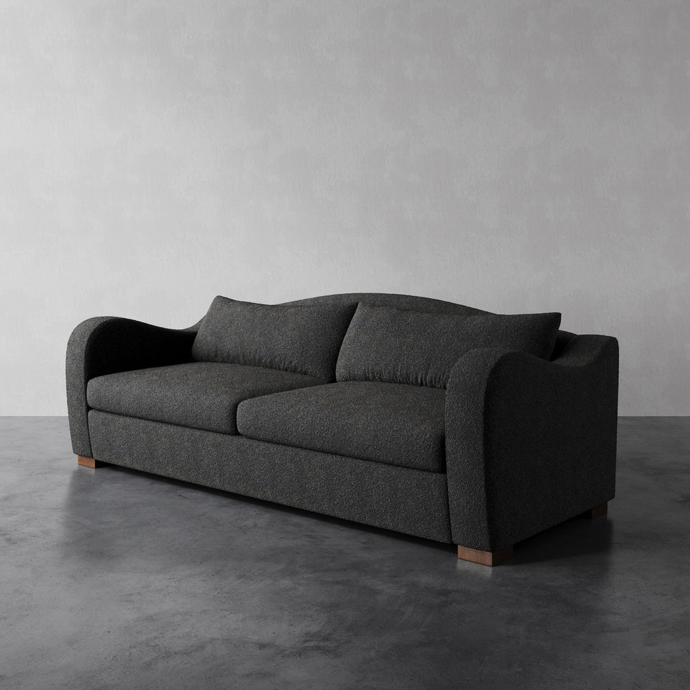 Lemieux et Cie Elodie Sofa in charcoal upholstery, deep-seat sofa with swooping arms and tailored cushions, shown on concrete floor against neutral studio backdrop.