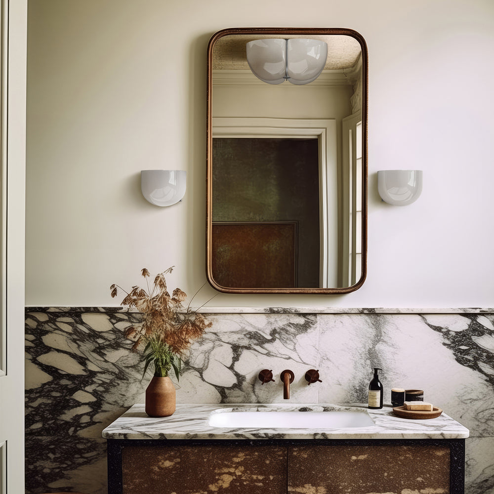 Lemieux et Cie Cheverny wall sconces in white, flanking a rounded mirror above marble vanity in a soft neutral bathroom with warm light.