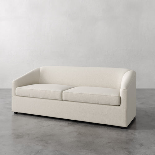 Lemieux et Cie Arvelle Queen Sleeper in ivory, low-profile sofa with rounded arms, shown on concrete floor against soft white wall.