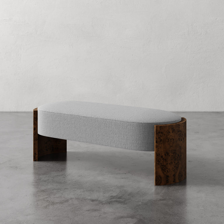 Lemieux et Cie Benoit Custom Upholstered Bench in gray upholstery with curved Maple burl legs, shown on polished concrete floor against neutral plaster walls.