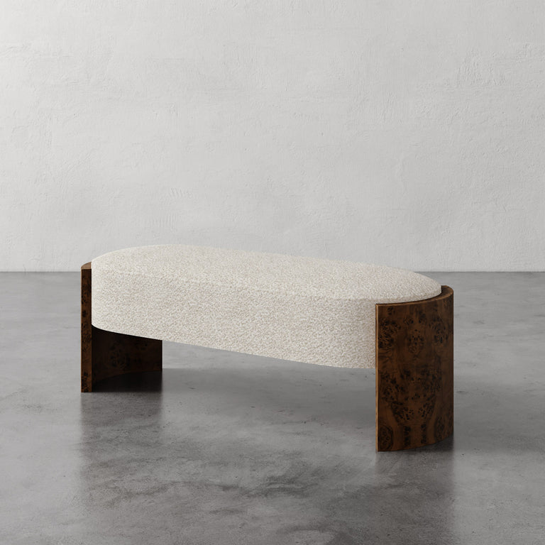 Lemieux et Cie Benoit Custom Upholstered Bench with curved Maple burl legs in warm finish and ivory upholstered seat, shown on concrete floor against textured plaster walls.