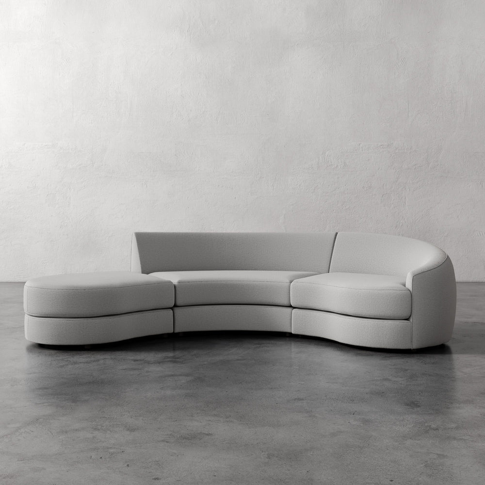 Lemieux et Cie Rulmann 3-Piece Right Sectional, sculptural curved sofa with rounded arms and low back, shown on concrete floor against plaster walls.