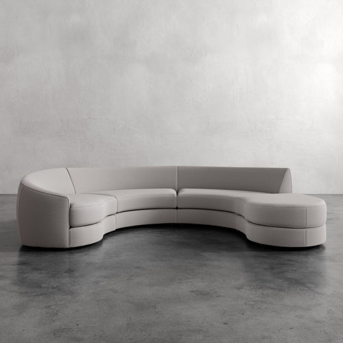 
Lemieux Et Cie Rulmann 4-Piece Left Sectional Modern curved sofa in a minimalistic setting with a plain wall and concrete floor.