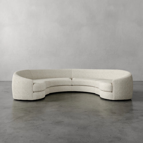 Lemieux Et Cie Rulmann 4-Piece Sectional  Curved beige sofa on a gray floor with a plain gray wall background