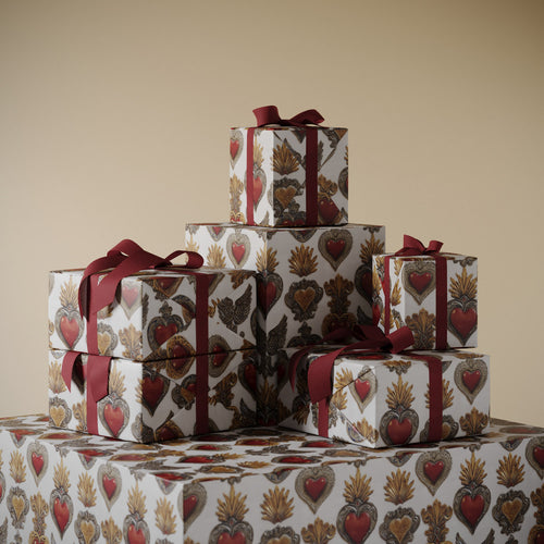 Lemieux et Cie Corazon Sagrado Gift Wrapping Paper stacked as wrapped boxes with deep red ribbon, shown on neutral surface against warm walls.