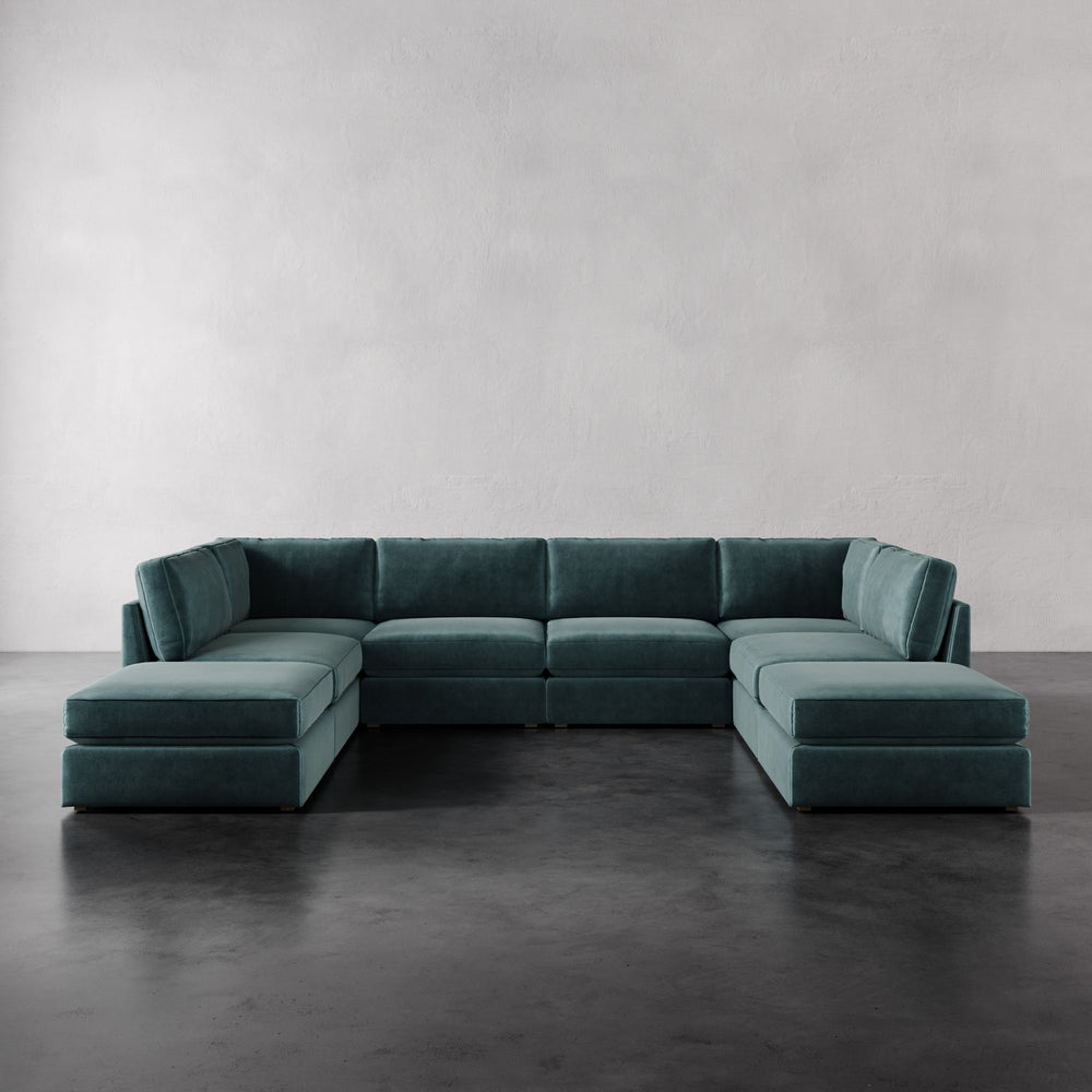 Lemieux et Cie Chanaux 8-Pc Sectional in deep teal, modular U-shaped sofa with dual chaises on dark concrete floor against white walls.