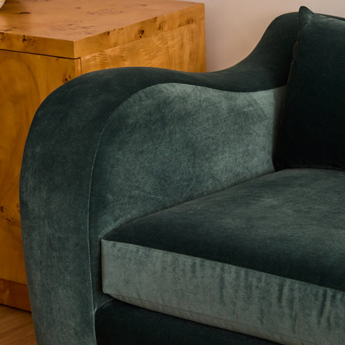 Green velvet armchair in a room with wooden furniture.