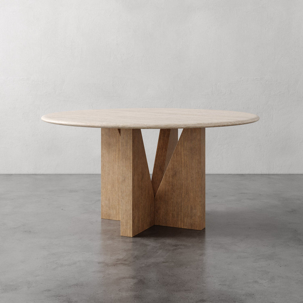 Lemieux et Cie Elysées Dining Table in oak with walnut finish, round dining table with geometric cross base, on polished concrete floor against white walls.