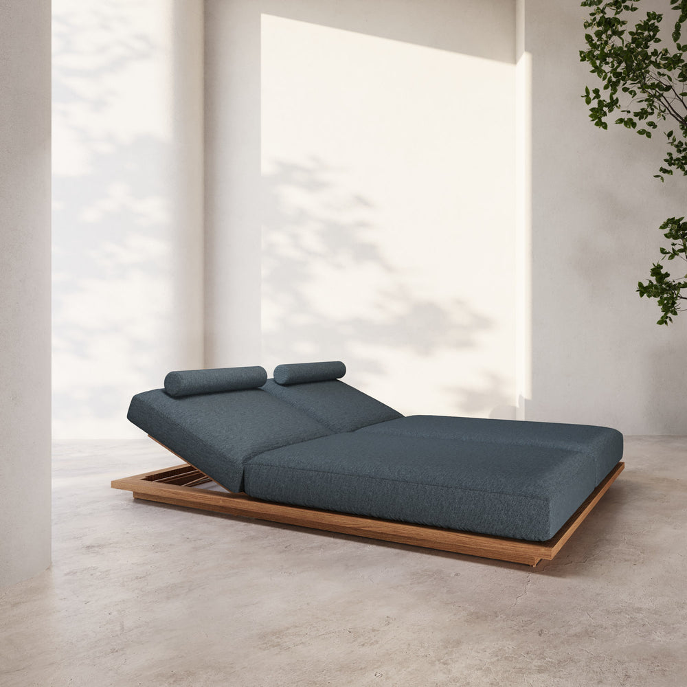 Lemieux et Cie S2 Teak Double Chaise Lounge in charcoal upholstery with teak wood base, outdoor daybed shown on concrete flooring in soft natural light.