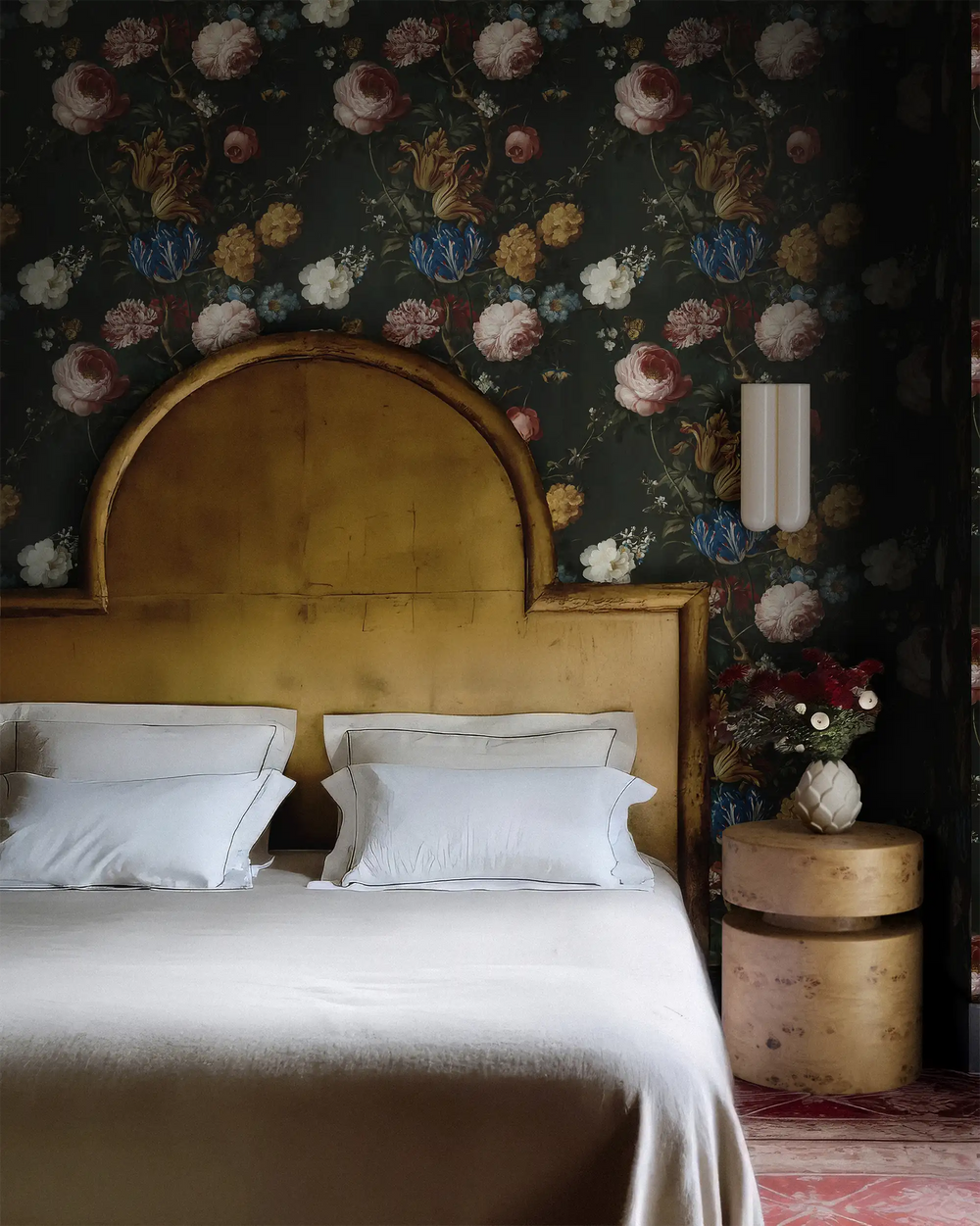 Lemieux et Cie Dutch Rose Wallpaper in dark floral chinoiserie, peel and stick wallpaper on gold-iridescent paper, shown in bedroom with rounded headboard and crisp white bedding.