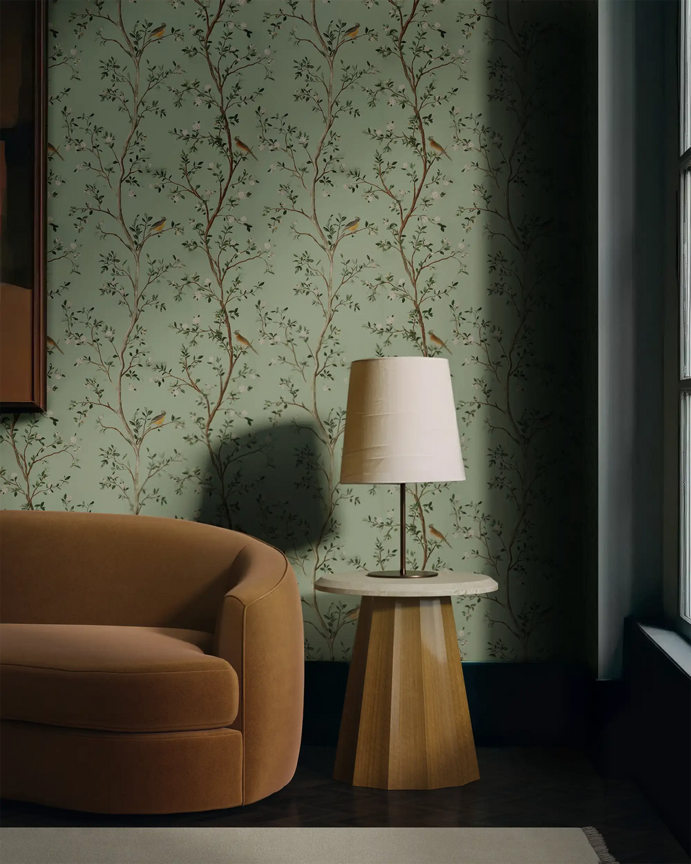 Living room styled with Lemieux et Cie Edelweiss light green chinoiserie peel and stick wallpaper, featuring white blossoms and songbirds in a modern chinoiserie design, paired with a brown sofa and table lamp.